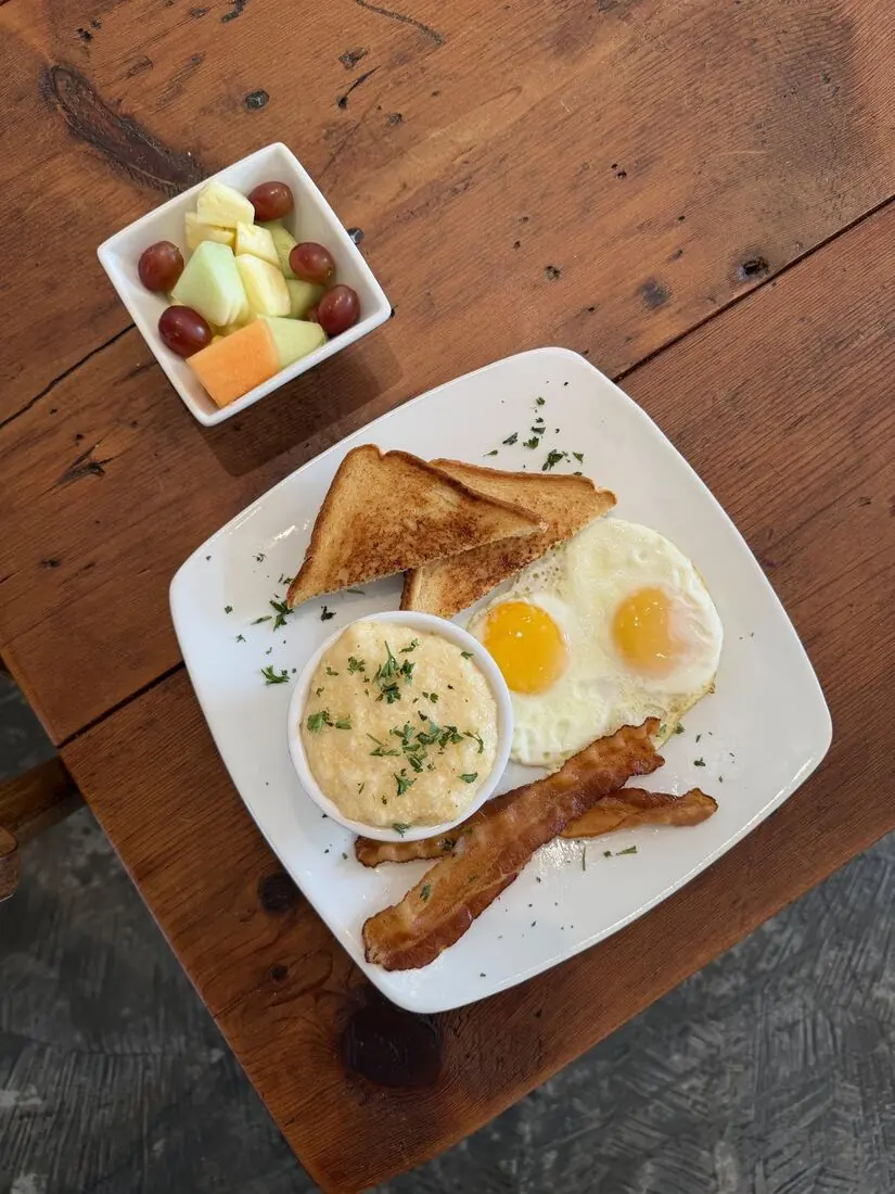 The Classic breakfast: eggs, bacon, grits, toast and fruit on a rustic table